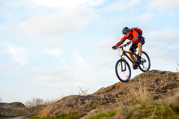 Fototapeta na wymiar Cyclist in Red Jacket Riding the Bike Down Rocky Hill. Extreme Sport Concept.