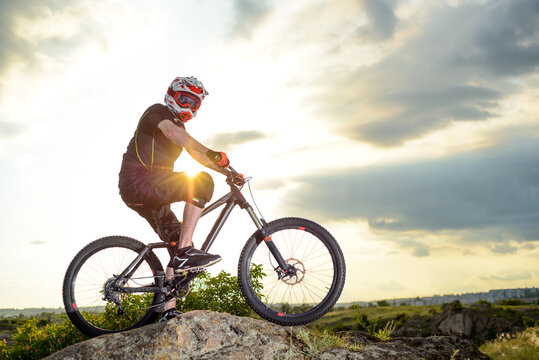 Professional Down Hill Cyclist Resting with Bike on the Rock at Sunset. Extreme Sport Concept.