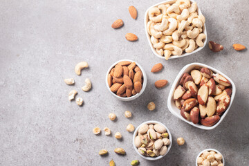 Large assortment of nuts in different bowls on stone table.