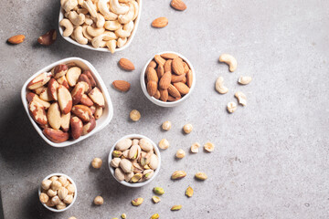 Large assortment of nuts in different bowls on stone table.