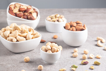 Large assortment of nuts in different bowls on stone table.