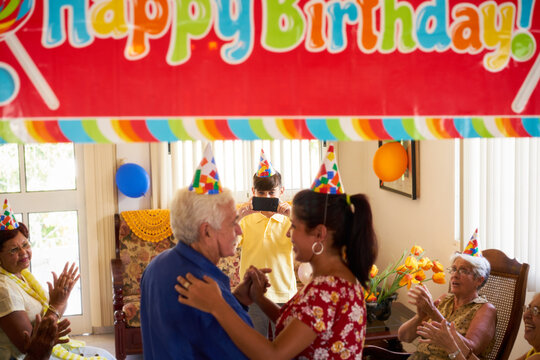 Family celebrating senior man birthday in hospice. Patient dancing with daughter in hospital and child taking photo.