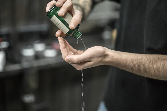 Green bottle with the lotion in the man's hands on the blurry background of the barbershop. Guy is pouring the lotion on his hand. Closeup. Horizontal.
