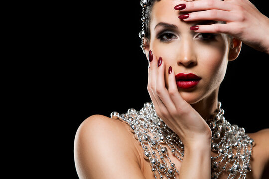 beautiful woman with dark makeup and red lipstick posing on black background. Wearing silver disco ball jewllery.