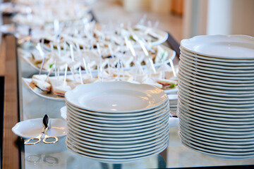 a stack of white plates on a glass banquet table against the background of the dishes with small...