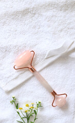 Rose quartz facial roller. Roller for cosmetic facial massage, chamomile and white towel. Flat lay on a light background. Top view, copy space