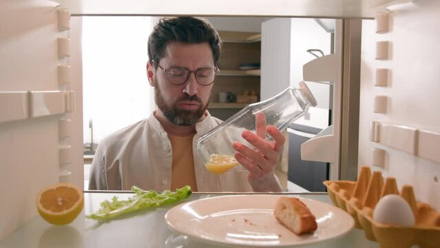 Man open empty refrigerator with half lemon lettuce leaf one egg slice of bread leftover orange juice in bottle find solution order food delivery with mobile phone app point of view from inside fridge
