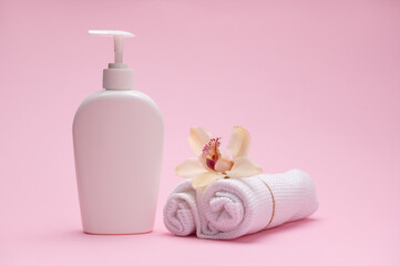 White cosmetic bottle mockup, orchid flower on rolled white waffle towels, isolated on pink background. Beauty blogging