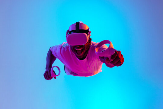 african american male gamer in virtual reality glasses flies in air and falls in neon lighting, guy levitates with vr