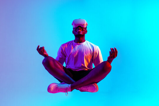 african american man meditates in virtual reality glasses and sits in the air in neon lighting - Powered by Adobe