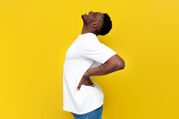 african american man in white t-shirt holding on to his back and bending over yellow isolated background