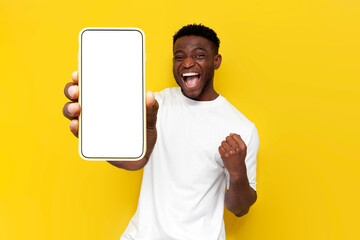 african american man in white t-shirt celebrating victory and showing blank screen of smartphone