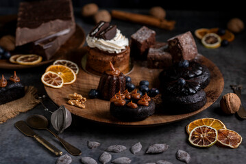 cakes puddings and chocolate muffins with blueberries and cream cherries and slices of dried citrus on highly decorated wooden plate.