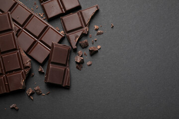 Pieces of delicious dark chocolate bars on black background, flat lay. Space for text