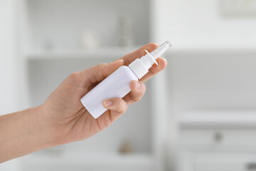 Woman holding nasal spray bottle indoors, closeup