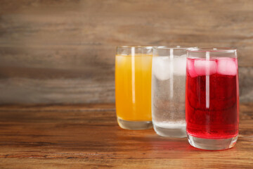Glasses of different refreshing soda water with ice cubes on wooden table. Space for text