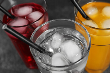 Glasses of different refreshing soda water with ice cubes and straws on grey table, view from above
