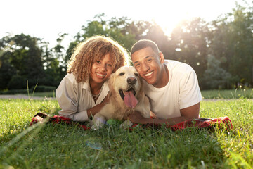 african american guy with girl lie together with golden retriever in the park in summer