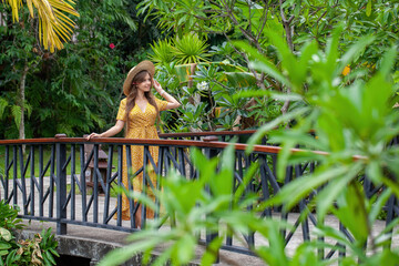 Obraz premium Beautiful female model with long hair stands alone in a lush green garden. Tropical vacation.