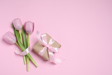 Obraz na płótnie Canvas Beautiful gift box with bow and tulips on pink background, flat lay. Space for text
