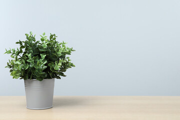 Beautiful artificial plant in flower pot on wooden table against light grey background, space for text
