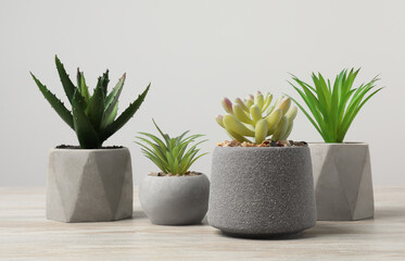 Many different artificial plants in flower pots on wooden table against light grey background