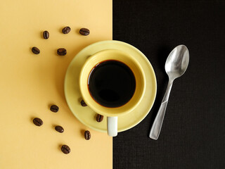Creative morning layout made of yellow coffee cup, coffee beans and silver teaspoon against yellow...