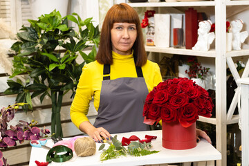 Floristry. Flowers. A florist girl at her desk, with a laptop and tools, collects a flower arrangement. Against the background of a showcase with garden decor.
