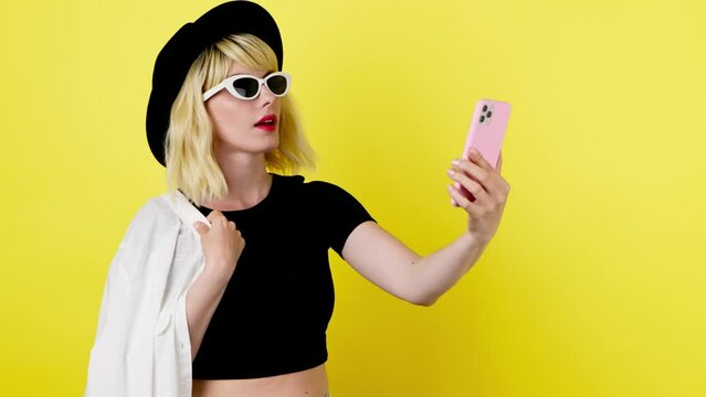 Selfie, pose and fashionable hipster woman with phone, peace sign for social media post. Lady with mobile smartphone posing, taking profile picture, trendy makeup, outfit, studio yellow background