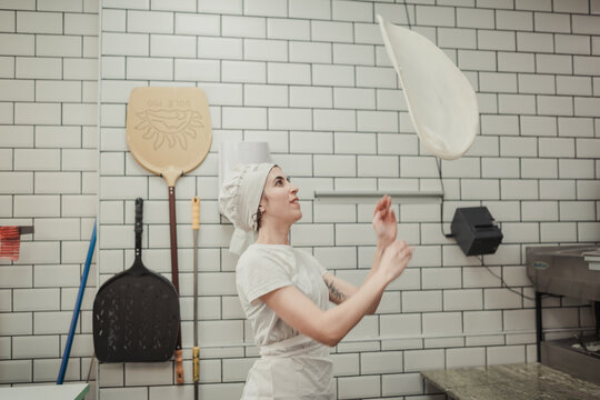 Woman playing with a pizza dough in a restaurant kitchen