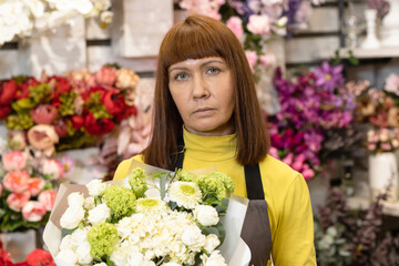 Floristry. Flowers. A florist girl with a bouquet of flowers, in a store, against the background of a showcase with garden decor.