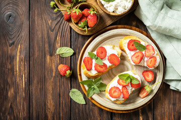 Sandwich with strawberries and soft cheese on wooden background. Berries toast breakfast, healthy food. View from above.