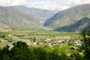 The landscape of the Caucasus Mountains and the village in the mountains on the background of a blue sky with clouds.