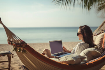 Woman uses her laptop outdoors in a hammock on the beach while on vacation