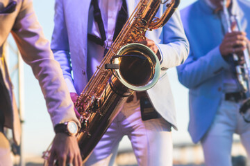 Concert view of saxophonist in a blue and white suit, a saxophone sax player with vocalist and musical band during jazz orchestra show performing music on stage in the scene lights