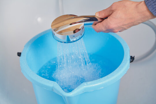 Hands pour water into plastic bucket through hose with nozzle