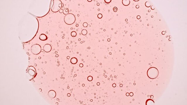 Transparent cosmetic pink gel fluid with molecule bubbles oil spreading on a white background. Macro Shot of Natural Organic Cosmetics, Medicine. Production Close-up. Slow Motion. 4k. High quality