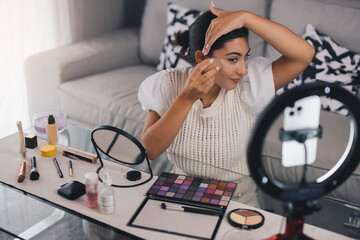 Young female beauty blogger applying foundation while shooting video