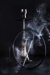 Hookah with a glass flask and a metal bowl on a black background with a copy space. Vertical photo.