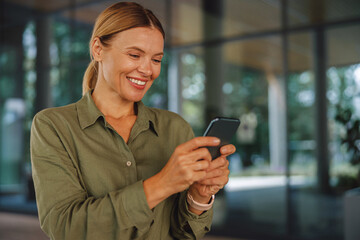 Smiling woman entrepreneur using phone whiile standing on modern building background 