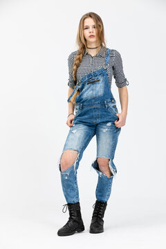 A girl dressed in ragged jeans poses for a photo shoot against a white background.
