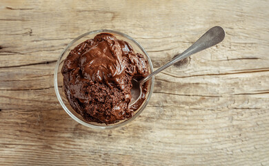 Transparent bowl with chocolate mousse, traditional French dessert and teaspoon on wooden background, top view