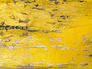 Old peeling wooden lath painted with yellow paint, close-up, top view. The surface of the lath is cracked, worn, with large and small cracks.