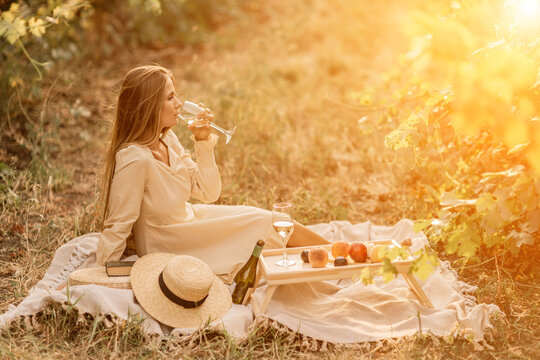 Woman picnic vineyard. Romantic dinner, fruit and wine. Happy woman with a glass of wine at a picnic in the vineyard on sunny day, wine tasting at sunset.