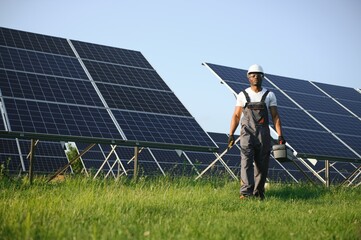 African american man in white helmet and grey overalls standing among rows of solar panels