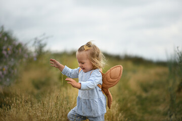 Little beautiful girl inraet in the field in summer. Baby in angel wings. child playing