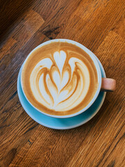Cup of freshly made delicious cappuccino coffee with oat milk with latte art on wooden background, top view.