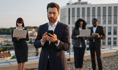 Caucasian bearded entrepreneur dialing number on smartphone while his business partners using...