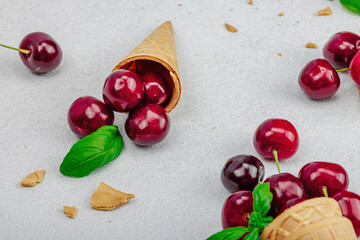 Ripe sweet cherries in waffle cones on light stone concrete background. Flat lay, vintage napkin