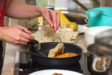 a woman is frying pita bread stuffed with vegetables and meat in a frying pan